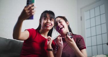 Handheld low angle view shot, Two Asian siblings sit on a sofa and use cell phone to talk to friends via call in a cozy living room. Share good times video
