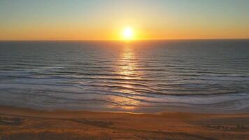 Flying over calm ocean at sunset with glowing waves and peaceful sandy beach video