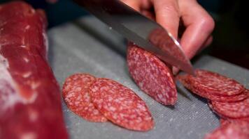 cut salami with a sharp knife in the kitchen. The process of slicing sausages with precision, displaying uniform cuts ideal for appetizers, side dishes, or recipes. Sausage slicing in close-up. video
