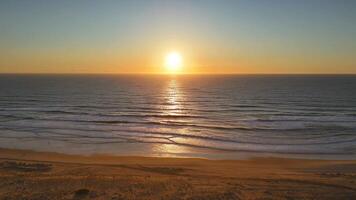 Golden sunset over ocean with drone view flying above empty and peaceful beach video