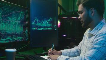 Indian Arabian man writing notes notebook working with pc computer trader programmer coder hacker male complete finish work online businessman night business office ethnic guy stretch hands relaxing video