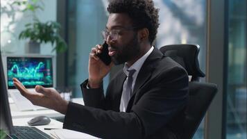 African American man businessman talking mobile phone call cellphone discuss with client consult check information computer documents problem male guy business manager employee entrepreneur in office video