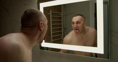 In a modern bathroom a muscular man grimaces in the mirror while sticking out his tongue showing a playful side during his daily grooming. The moment captures humor and confidence video