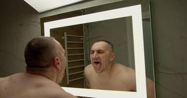 man with a muscular build stands shirtless in front of a bathroom mirror grimacing and sticking out his tongue video