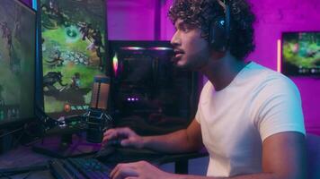 Focused Arabian Indian Latino man talking speaking playing game gamer computer tech happy male smiling guy presenter in headphones streamer home neon blog vlog pc streaming online web host hobby video
