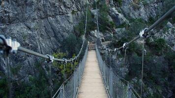 Rugged suspension bridge spanning deep rocky gorge, connecting distant cliff sides with wooden planks and steel cables, revealing breathtaking wilderness landscape video