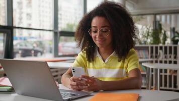 African American girl student gadget addict using mobile phone chatting social media looking in smartphone in university beautiful ethnic woman female exam preparations study with laptop education video