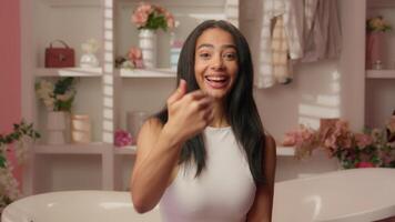 Smiling positive friendly Hispanic woman teenager girl cheerful happy female in pink bathroom pointing finger at camera come here invite you welcome inviting calling alluring skincare beauty concept video