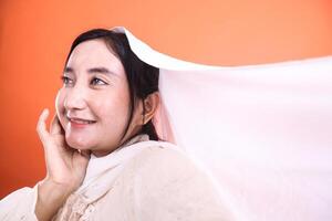 Smiling Asian Woman with Flowing White Fabric A Moment of Serenity. Captured gracefully, the portrait is isolated on a orange background. photo