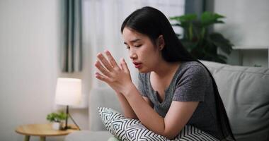Handheld steady shot, Asian woman sit on the sofa alone, lost in thought. Her brows were slightly furrowed and expression tense in the quiet atmosphere at home video