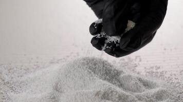 Black gloved hand pouring white plastic granules onto a pile in soft industrial lighting, Close-up of raw polymer material handling during precision manufacturing processes video