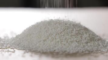 White plastic granules falling onto a growing pile in a bright industrial setting, Close-up of raw polymer material used in injection molding or component manufacturing video
