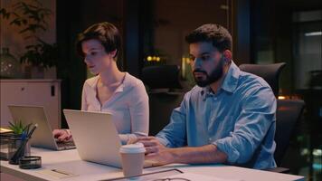 profissional equipe colegas de trabalho multirracial o negócio homem mulher dentro Sombrio noite escritório digitando laptops indiano homem de negocios caucasiano empresária computador programação dois empregados gerentes trabalhando hora extra video