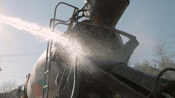 Water sprays from hose to clean cement mixer after concrete unloading, Close-up of construction equipment maintenance under bright daylight during site operations video