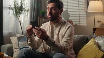 Frustrated sad Caucasian man homeowner businessman upset disappointed male guy browsing mobile phone internet on home couch sofa smartphone receive message bad news worried scam failure in living room video