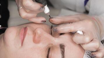 Permanent eyelash line tattoo procedure in progress, cosmetologist applies pigment between lashes using professional tattoo device during close-up eye treatment video
