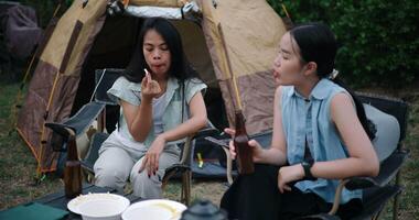 Handheld shot, Two Asian friends sit on chairs and talk happily in front of a tent in a camping atmosphere. Holiday Activities video