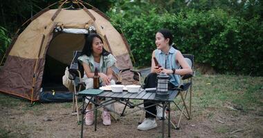 Handheld wide shot, Two Asian women sit together in a garden, happily chatting while enjoying snacks and drinks, surrounded by a cozy camping vibe. Holiday Activities video