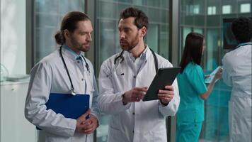 Experienced Caucasian two men doctors clinician surgeon pediatrician physician in labcoat stethoscope examining patient health test result using digital tablet diagnostic treatment at hospital clinic video