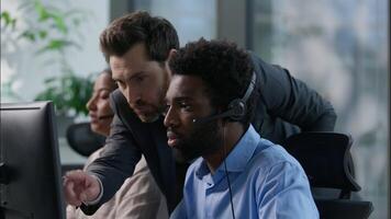 Friendly Caucasian boss business man businessman explain encourage African American worker call center operator work computer headset client help line customer support multiethnic teamwork callcenter video