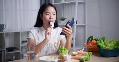 Handheld shot, Beautiful Asian woman enjoys eating fruit while happily calling with friends on mobile phone at home. Relax at home, Enjoy healthy food video