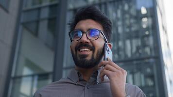 Close up happy smiling Arabian Indian man successful businessman ethnic guy talking mobile phone outdoors male employer chatting with business client talk smartphone in city call cellphone negotiate video