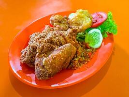 Ayam Geprek with Fried Tofu and Vegetables on Orange Plate photo