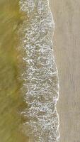Overhead View of Gentle Waves on Sandy Beach. Aerial perspective of small waves creating intricate patterns of foam as they wash over a sandy shoreline, evoking video