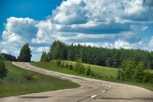 A scenic winding road through lush green countryside under a bright blue sky with clouds. photo