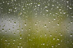 Raindrops cascade down a window, creating a tranquil view with a blurred green backdrop. photo
