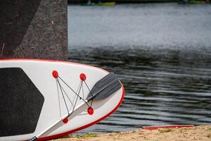 A paddleboard and paddle rest on the sand near calm water, ready for a summer adventure. photo