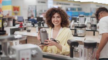 Young couple browsing kitchen appliances in electronics store, examining food processor, sharing joyful moments while making purchasing decision in slow motion video