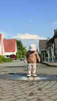 In a cheerful neighborhood, a joyful toddler splashes in a shiny puddle under warm sunshine, enjoying carefree moments of innocent childhood play and exploration video