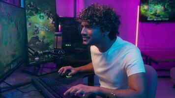 Indian Arabian Latino man playing computer pc technology game cyberspace tournament esport championship smile virtual monitor player networking online typing fun pleasure looking at camera male guy video