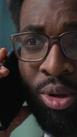 Close up face professional worker African American man businessman talking mobile phone cellphone call consulting client male business manager employee guy looking at monitor computer solve in office video