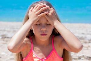 Caucasian child of 8 9 years with closed eyes holding hands on forehead feeling headache because of heatstroke on sea beach photo