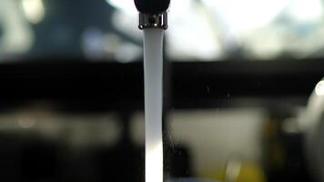 Sunlight illuminating clear, transparent water streaming from gleaming chrome faucet spout, cascading with purity against softly blurred kitchen interior background video