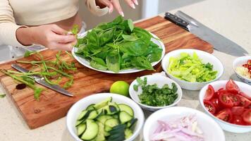 Hands preparing fresh basil with assorted vegetables on a cutting board in a bright kitchen setting video