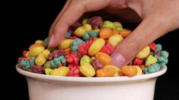 A hand reaches into a bowl of colorful cereal against a black background, highlighting vibrant colors and textures video