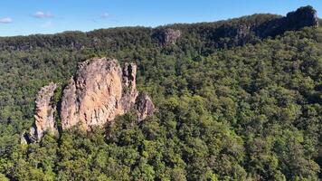 Drone footage captures the iconic Nimbin Rocks surrounded by dense greenery under clear blue skies video