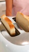 Slices of bread rise from a toaster in a bright kitchen. A person stands nearby, creating a warm, domestic atmosphere video