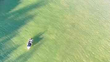 Drone captures a boat navigating tranquil, clear waters with shifting shadows and sunlight video