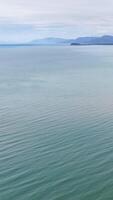 Calm ocean waters stretch towards distant mountains under a cloudy sky, creating a tranquil and expansive scene video