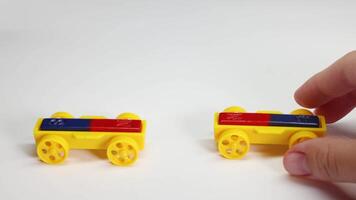 Hands manipulate magnetic toy cars on a white surface, illustrating magnetic attraction and repulsion with colorful components video
