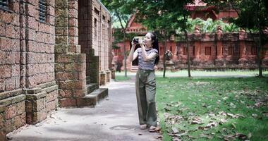 Happy young woman is enjoying a quiet stroll, taking photos of old sculptures and ancient brick structures, Enjoy holiday travel. video