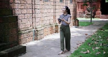 Handheld shot, Happy young woman is enjoying a quiet stroll, taking photos of old sculptures and ancient brick structures. video