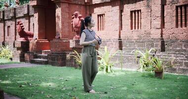 Handheld shot, Happy young woman is enjoying a quiet stroll, taking photos of old sculptures and ancient brick structures, Enjoy travel. video