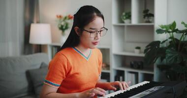Handheld shot, Young Asian woman is relaxing and enjoying playing music on an electronic keyboard in a quiet house. Leisure activities video