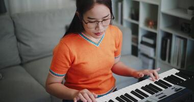 Handheld high angle view shot, Young woman is relaxing and enjoying playing music on an electronic keyboard in a quiet house. Leisure activities at home video