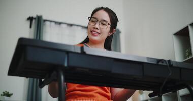 Low angle view shot, Beautiful Asian woman playing the keyboard with happy smile in cozy living room at home. Enjoy a relaxing weekend activity video